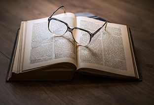 Un livre ouvert et des lunettes de vue posées dessus.