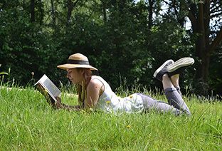 Jeune femme portant un chapeau allongée dans l'herbe et lisant un livre.